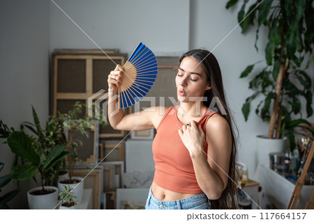 Tired unhappy overheated woman fanning herself suffering from summer heat, uncomfortable sensations Tired unhappy overheated woman fanning herself suffering from summer heat, uncomfortable sensations 117664157