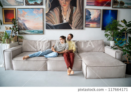 Happy relaxed loving couple rest on couch in home art gallery hugging dreaming looking aside window Happy relaxed loving couple rest on couch in home art gallery hugging dreaming looking aside window 117664171