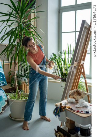 Positive optimistic woman painter embodies creative ideas expresses bright emotions in picture. Positive optimistic woman painter embodies creative ideas expresses bright emotions in picture. 117664172