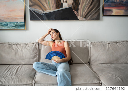 Tired unhappy overheated woman fanning herself suffering from summer heat, uncomfortable sensations 117664192