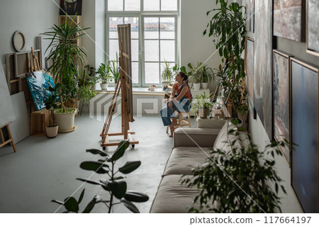 Thoughtful woman painter at art creative workshop workplace looking up with enthusiasm.  117664197