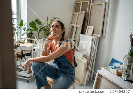 Happy thoughtful woman painter at art creative workshop workplace looking up with enthusiasm.  117664207