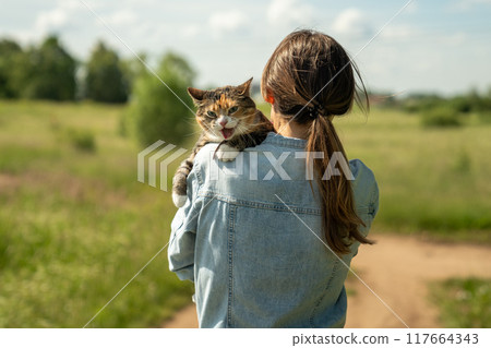 Cat on leash for first time outdoor sits on shoulder of loving owner, stressed, worried and afraid Cat on leash for first time outdoor sits on shoulder of loving owner, stressed, worried and afraid 117664343