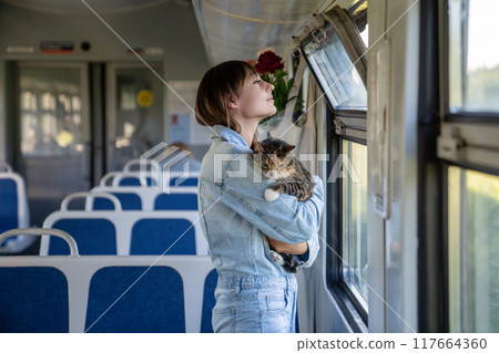 Cat traveling by train with owner. Woman cuddles her cat, soothing it from stress during train ride Cat traveling by train with owner. Woman cuddles her cat, soothing it from stress during train ride 117664360