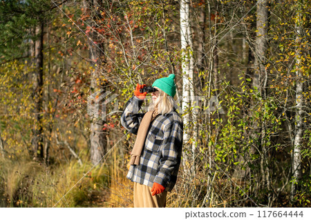 Enthusiastic woman with binoculars, studying birds and watching nature in sunny autumn woodland Enthusiastic woman with binoculars, studying birds and watching nature in sunny autumn woodland 117664444