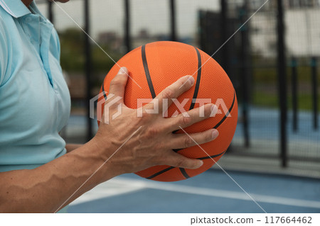 Sporty man holding orange basketball ball in hand and hope success on sports court. Focus on ball. Close up. Basketball coach. Sporty man holding orange basketball ball in hand and hope success on sports court. Focus on ball. Close up. Basketball coach. 117664462