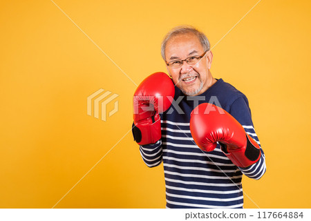 Portrait Asian old man wearing glasses wear two red boxing gloves studio shot isolated yellow background, smiling happy elderly man gray haired healthy fighter lifestyle concept 117664884