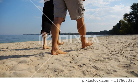 Bare feet of couple stepping together along beach at ocean background. Male and female legs of pair walking near sea. Happy lovers going on sandy shore. Concept of summer vacation or holiday. Bare feet of couple stepping together along beach at ocean background. Male and female legs of pair walking near sea. Happy lovers going on sandy shore. Concept of summer vacation or holiday. 117665385