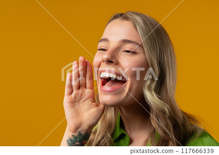 Attention, portrait of blonde young woman shouting, holding hand near open mouth Attention, portrait of blonde young woman shouting, holding hand near open mouth 117666339