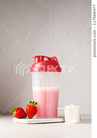 Pink strawberry protein drink shake in a shaker bottle and protein powder in a scoop. Food supplement. Pink strawberry protein drink shake in a shaker bottle and protein powder in a scoop. Food supplement. 117666477