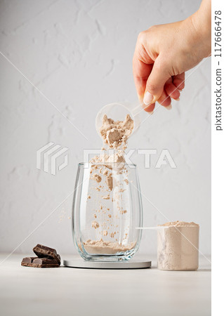 Protein powder in a scoop. Pouring chocolate protein powder in a glass. Food supplement. 117666478