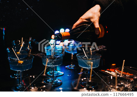 Bartender pouring cocktails over ice at a dimly lit bar. Nightlife, cocktail preparation, mixology, party atmosphere, bar scene. 117666495