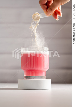 Collagen protein powder. Pouring protein pink powder in a glass.  117666502