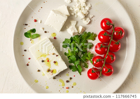 feta cheese, for salads, with cherry , green butter, greens, on a white plate, appetizer, top view, close-up, 117666745