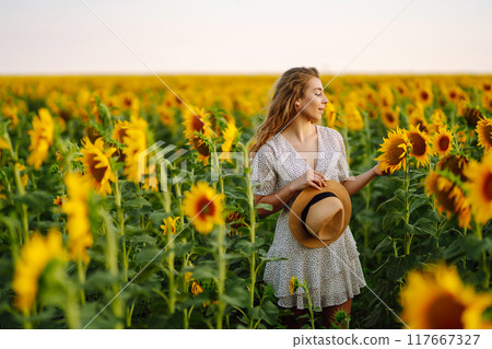 Beautiful woman strolling through field with sunflowers. Fashion, lifestyle, vacations concept. 117667327