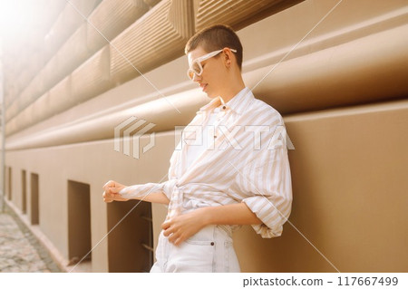 Hipster fashion woman in stylish glasses sits on a curb in the street in Europe. 117667499