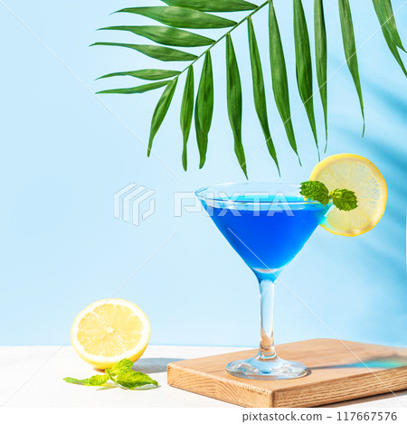Blue summer cocktail with lemon and palm leaf 117667576