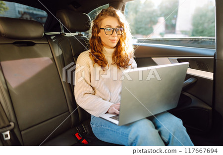 Business transportation. Woman with laptop works in back seat of car. Concept of transport. Business transportation. Woman with laptop works in back seat of car. Concept of transport. 117667694
