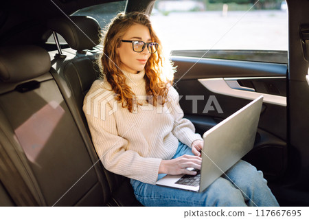 Business transportation. Woman with laptop works in back seat of car. Concept of transport. Business transportation. Woman with laptop works in back seat of car. Concept of transport. 117667695