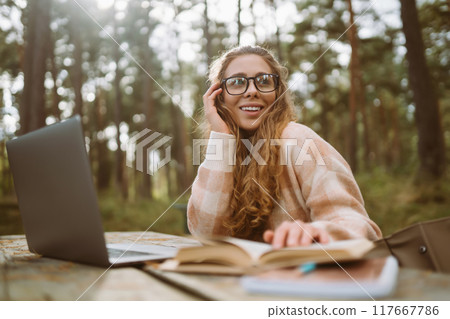 Beautiful woman working online or studying at laptop sitting at park. Freelance, education concept. Beautiful woman working online or studying at laptop sitting at park. Freelance, education concept. 117667786