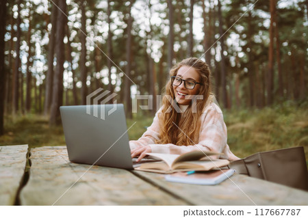 Beautiful woman working online or studying at laptop sitting at park. Freelance, education concept. Beautiful woman working online or studying at laptop sitting at park. Freelance, education concept. 117667787