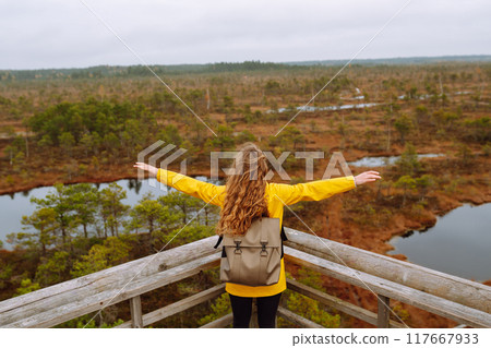 Young woman looks at amazing nature on observation deck. Tourist enjoys a view of magical swamps. 117667933