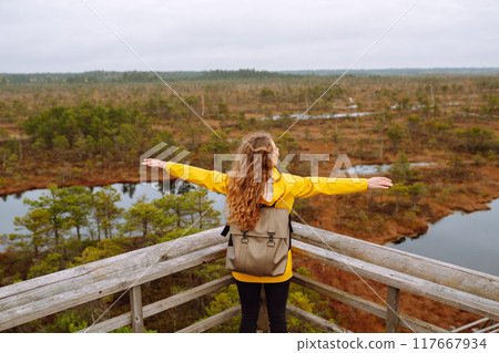 Young woman looks at amazing nature on observation deck. Tourist enjoys a view of magical swamps. 117667934