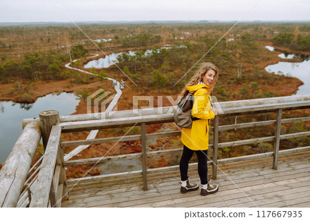 Young woman looks at amazing nature on observation deck. Tourist enjoys a view of magical swamps. 117667935
