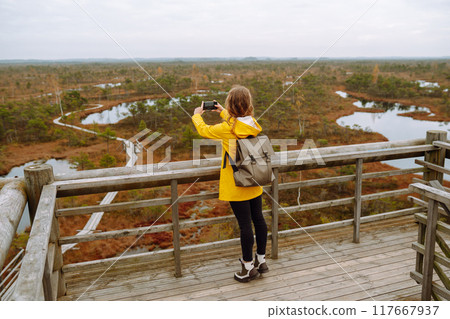 Young woman looks at amazing nature on observation deck. Tourist enjoys a view of magical swamps. 117667937