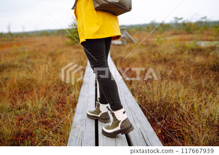 Close-up of legs in boots of woman tourist walking along wooden path against backdrop of wildlife 117667939
