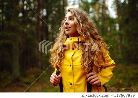 Traveler woman in yellow coat explores, walks through wild forest in nature. Vacation travel concept 117667959