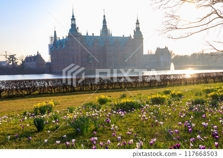 View of Frederiksborg castle in Hillerod, Denmark. Beautiful lake and garden with crocuses and daffodils on a foreground View of Frederiksborg castle in Hillerod, Denmark. Beautiful lake and garden with crocuses and daffodils on a foreground 117668503