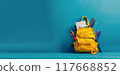 Yellow schoolbag on empty blue background. Orange bag with stationery and school accessories. Child backpack for learning 117668852