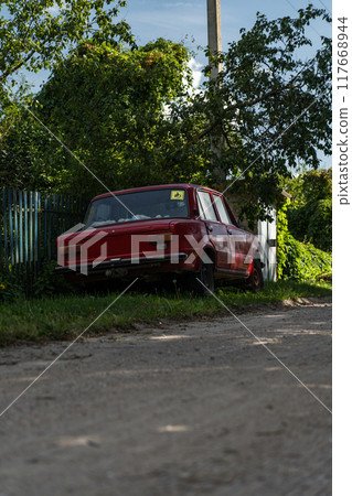 A red Soviet car is parked on the side of the road in the village A red Soviet car is parked on the side of the road in the village 117668944
