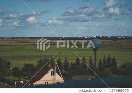 A village house, and behind it a large, green field. Thick clouds in the sky A village house, and behind it a large, green field. Thick clouds in the sky 117668965