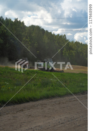 Two combines are working in the field, harvesting crops. Combines collect grain 117668999