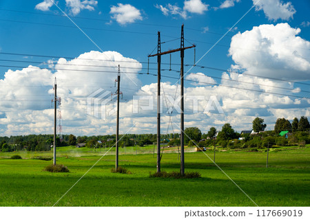 Supports of power lines in a green field. Clouds float across the sky Supports of power lines in a green field. Clouds float across the sky 117669019