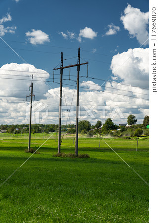 Supports of power lines in a green field. Clouds float across the sky Supports of power lines in a green field. Clouds float across the sky 117669020