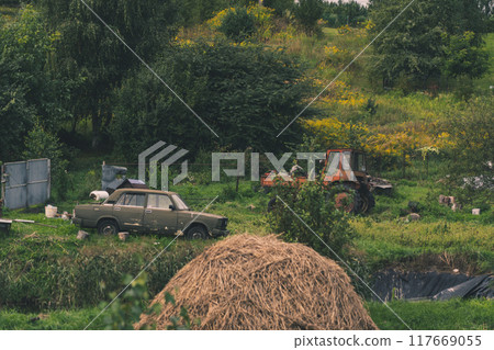 A rustic courtyard. A haystack. In the background is an old car and a tractor A rustic courtyard. A haystack. In the background is an old car and a tractor 117669055