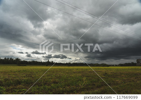 Clouds hung over the village and the green field. Support of power lines nearby 117669099