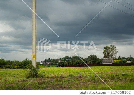 Clouds hung over the village and the green field. Support of power lines nearby Clouds hung over the village and the green field. Support of power lines nearby 117669102
