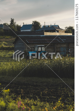 Blue tractor in the evening, at sunset after a hard day's work.A green field Blue tractor in the evening, at sunset after a hard day's work.A green field 117669175