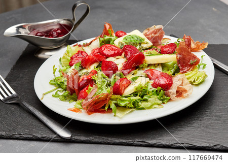 Salad with fresh strawberries, prosciutto, and mixed greens, topped with a light vinaigrette 117669474
