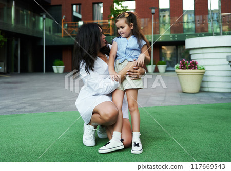 A woman kneels to talk to a young girl in a modern urban park during the afternoon 117669543
