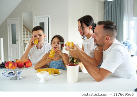 Family enjoying sweet corn together in a cozy dining room during a sunny afternoon Family enjoying sweet corn together in a cozy dining room during a sunny afternoon 117669566