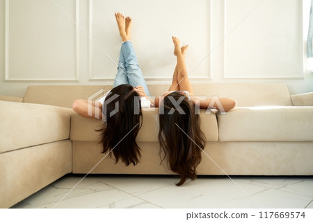 Friends relaxing on a couch with their feet against the wall in a modern living room during the day Friends relaxing on a couch with their feet against the wall in a modern living room during the day 117669574