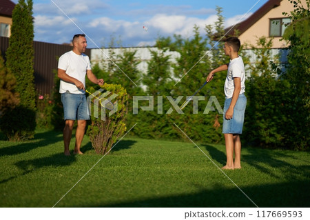 Father and son playing badminton together in a sunny backyard in summer Father and son playing badminton together in a sunny backyard in summer 117669593