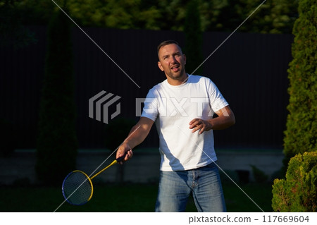 Man playing badminton outdoors in a garden during late afternoon 117669604