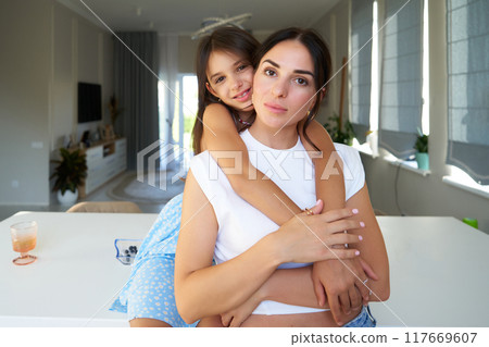 Mother and daughter embrace in a bright, modern kitchen during the afternoon 117669607