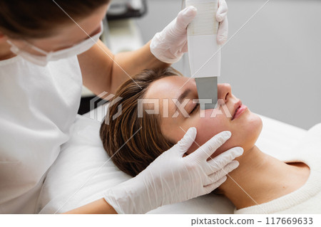 Aesthetician performing facial treatment on a client in a modern skincare clinic 117669633